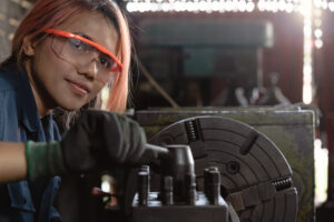 Certified industry female mechanical engineer working on industrial factory machinery - Skilled apprentice technician woman wearing safety equipment - Training, repair and diversity at work concept